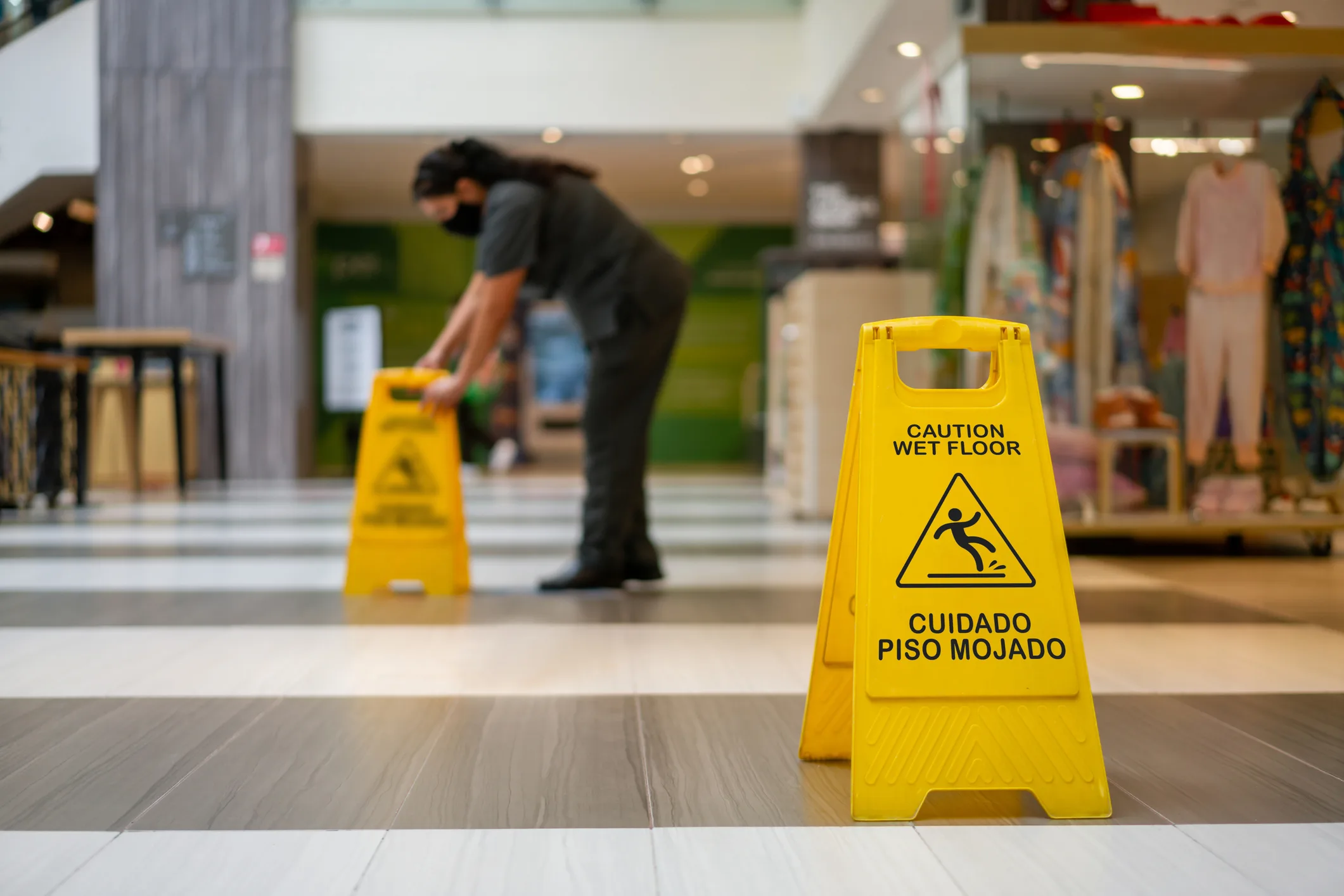 A crumpled milk carton lies in the middle of a large spill in front of grocery store dairy coolers, creating a slip hazard.