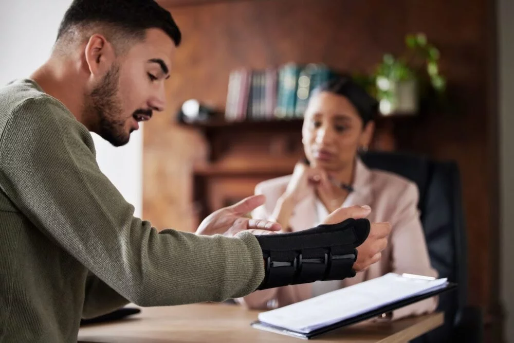A man with his arm and wrist in a brace discusses his injury with a personal injury lawyer in Greenwood.