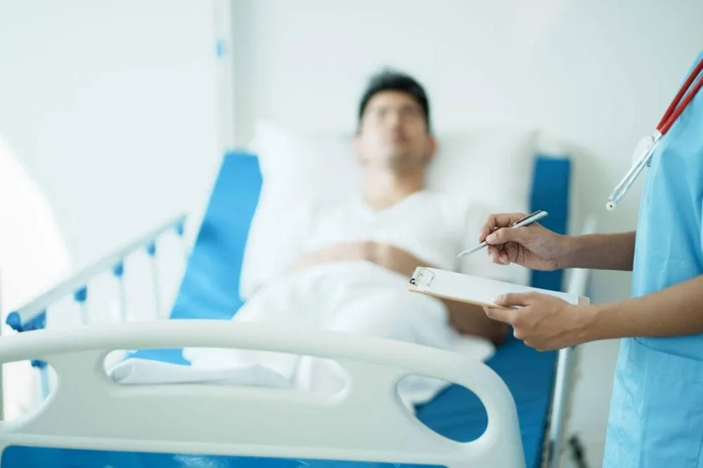 Close up of a doctor holding a clipboard beside a patient in a hospital bed.
