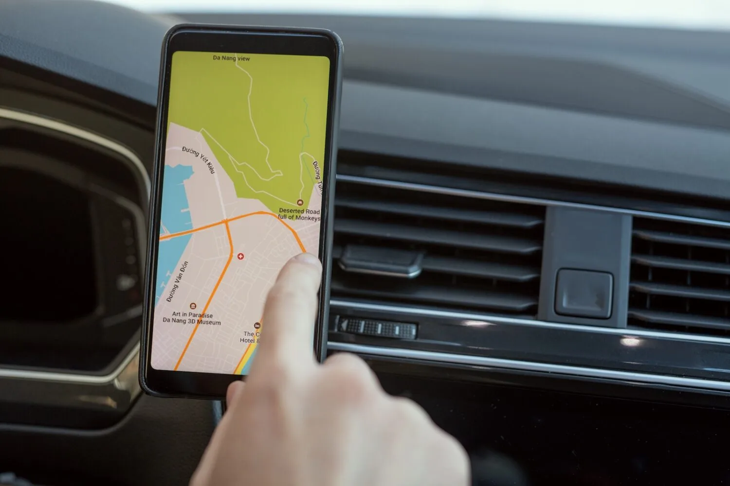 Hand of young man sitting in car and pointing at map on screen of smartphone.