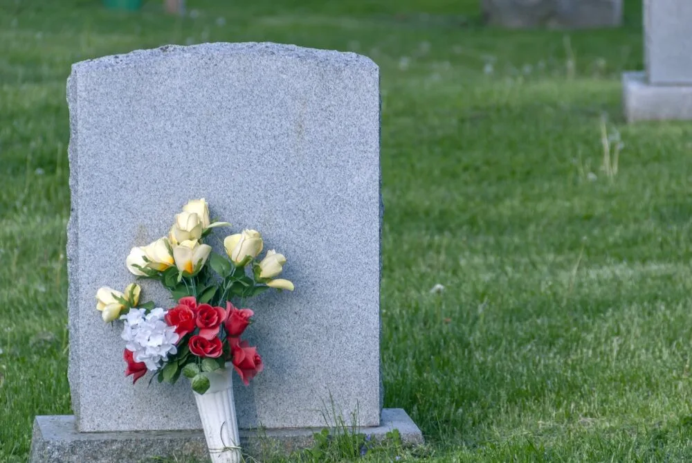 A bouquet of flowers leaning against a concrete gravestone.