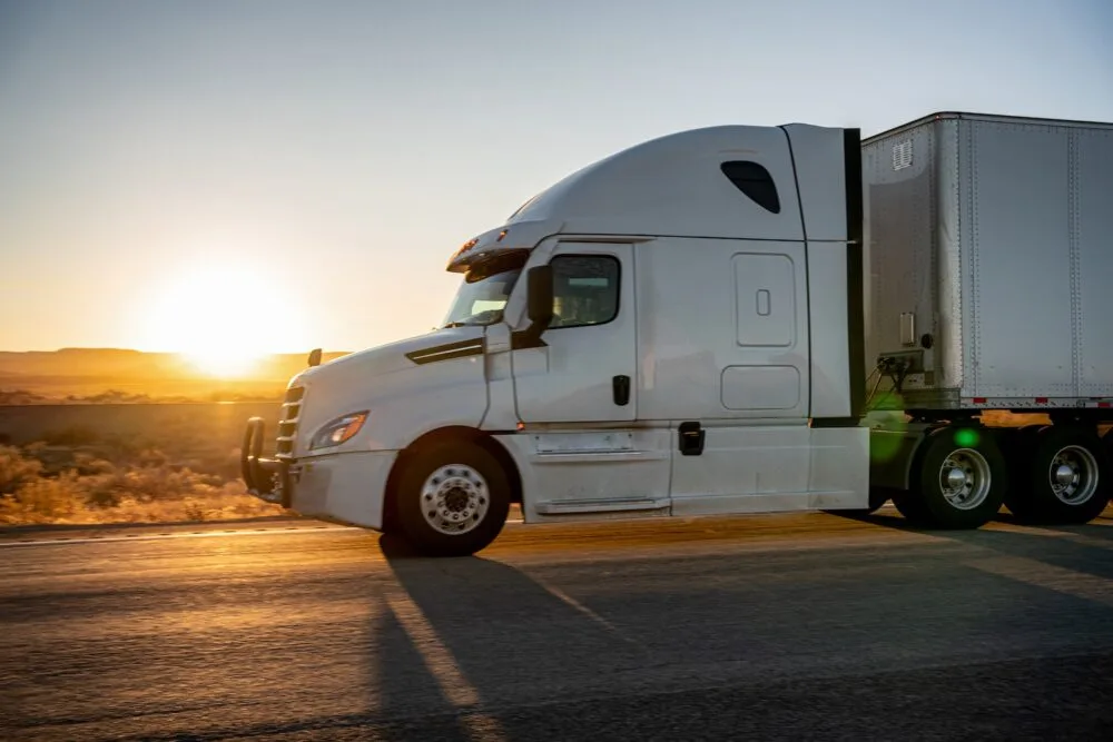 A white semi-truck driving down the highway at dusk.