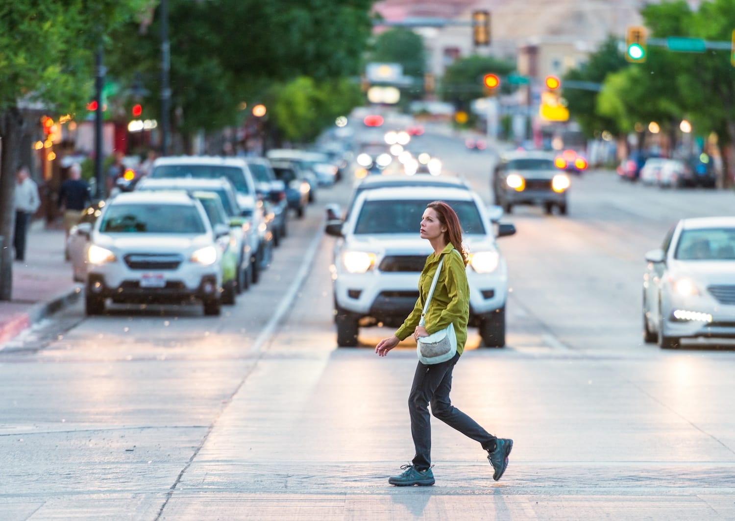 A woman crossing at a crosswalk on a busy street with cars in the background.