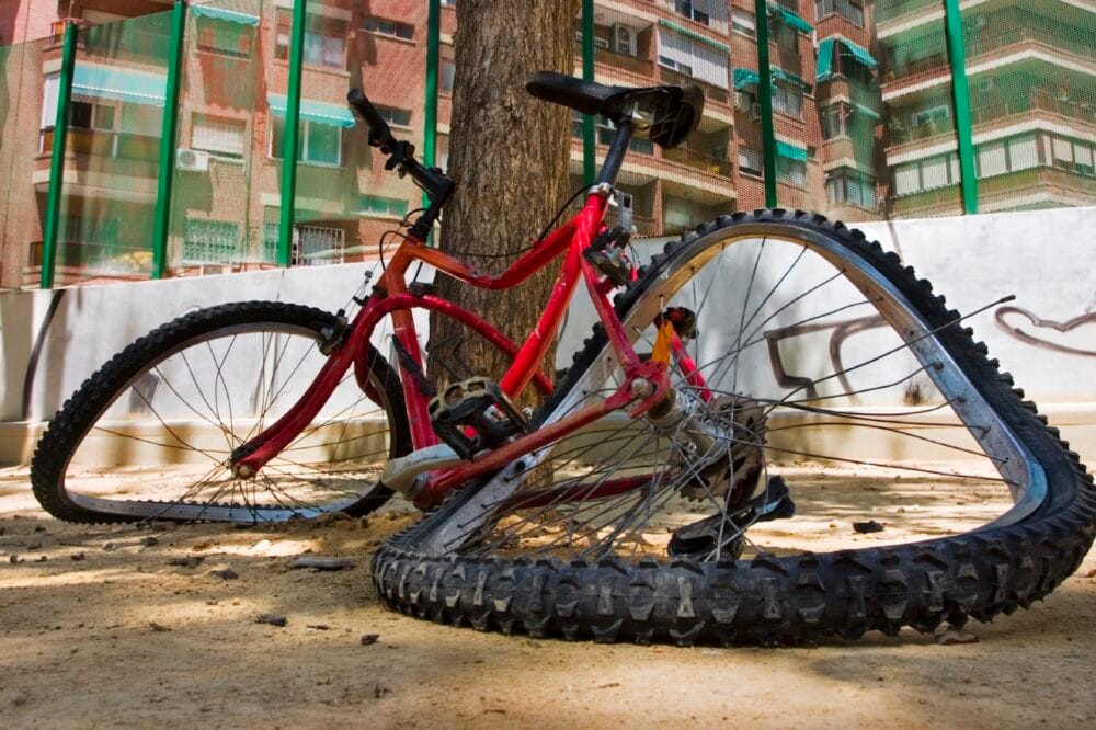 Red frame bicycle that’s been damaged in a bicycle accident. The wheels are warped and bent out of shape.