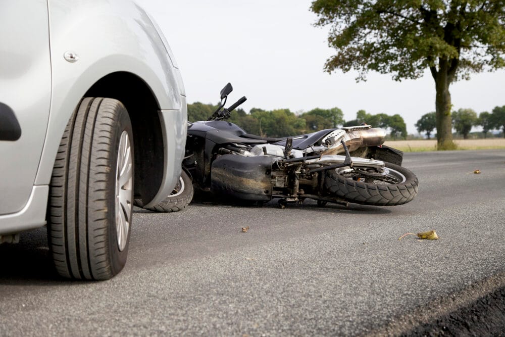 A motorcycle lying on its side on the road in front of a car after an accident.