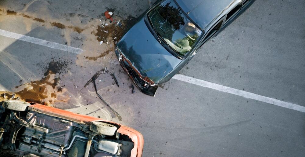 Aerial view of a car accident. One car is upside down, the other has significant damage to the front end.