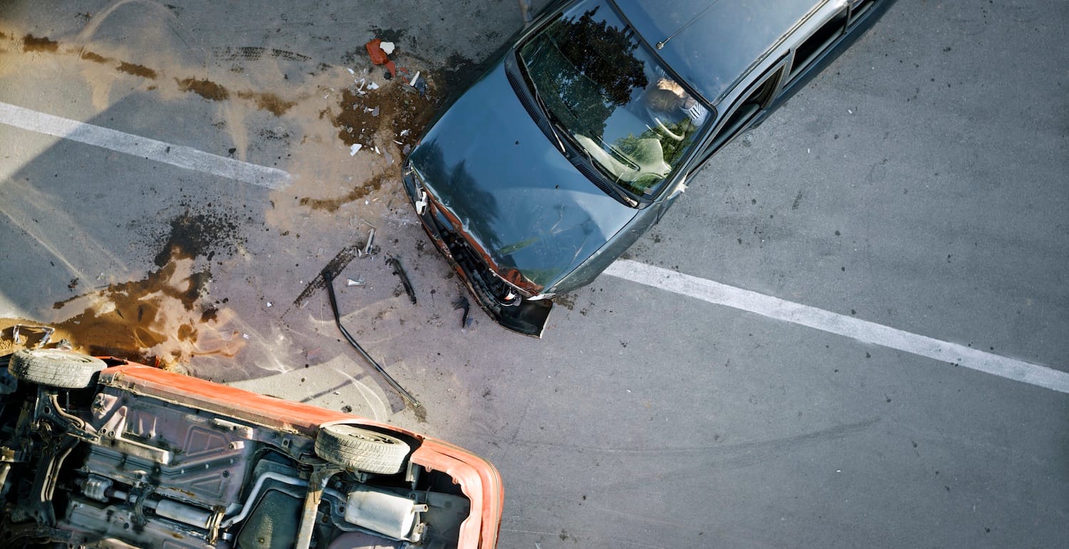 Aerial view of a car accident. One car is upside down, the other has significant damage to the front end.