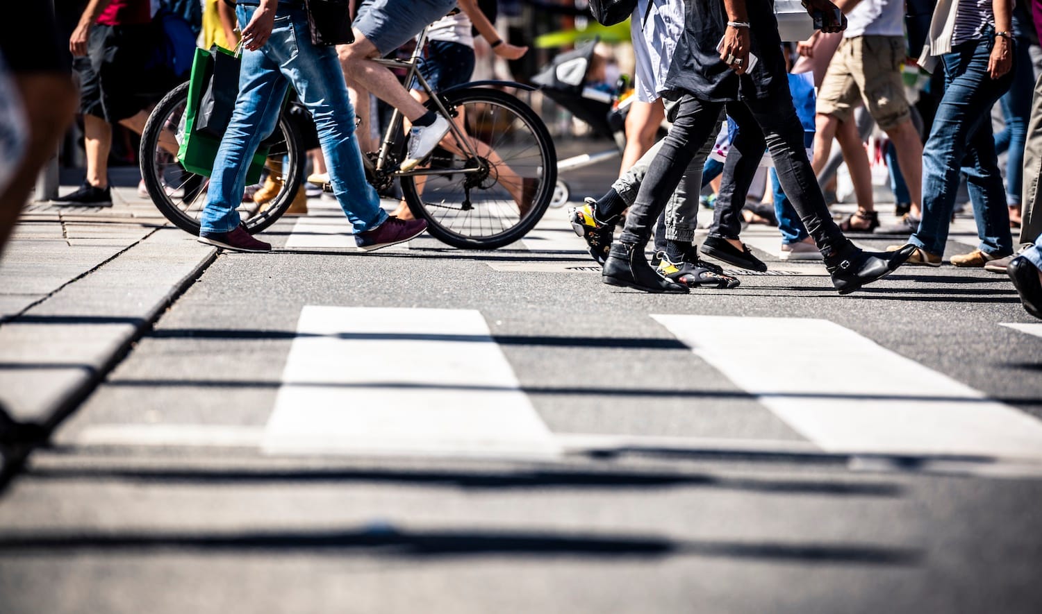Close-up of pedestrians crossing a busy city crosswalk with cyclists and other foot traffic in the background.