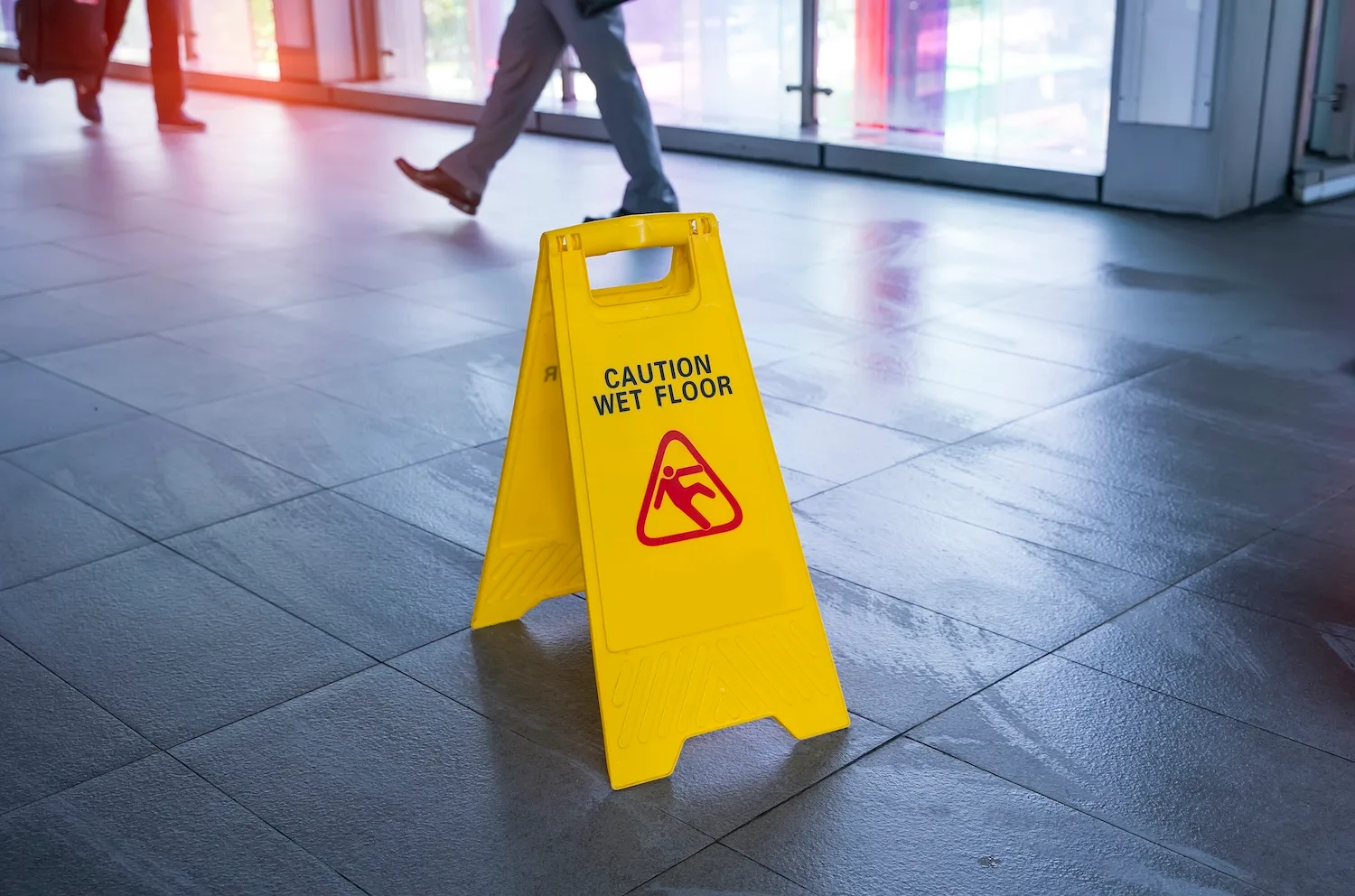 A recently mopped floor where people are walking, a wet floor sign is set up in the middle of the floor to warn people.