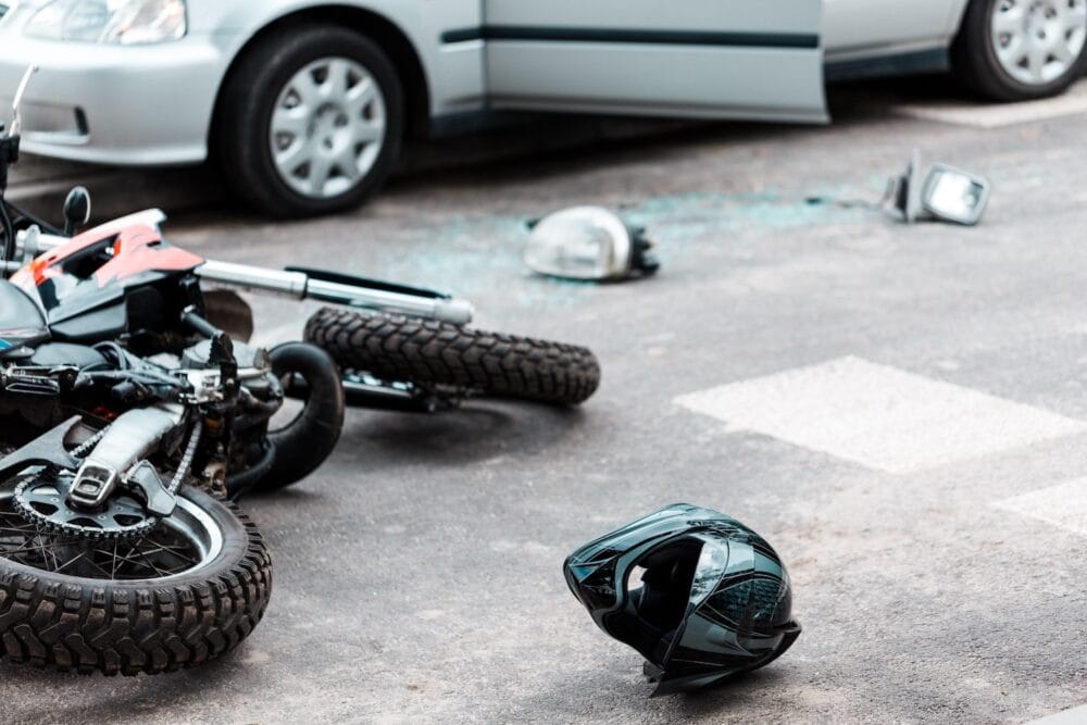A motorcycle helmet lying on the street with a motorcycle accident with a car is blurred in the background.