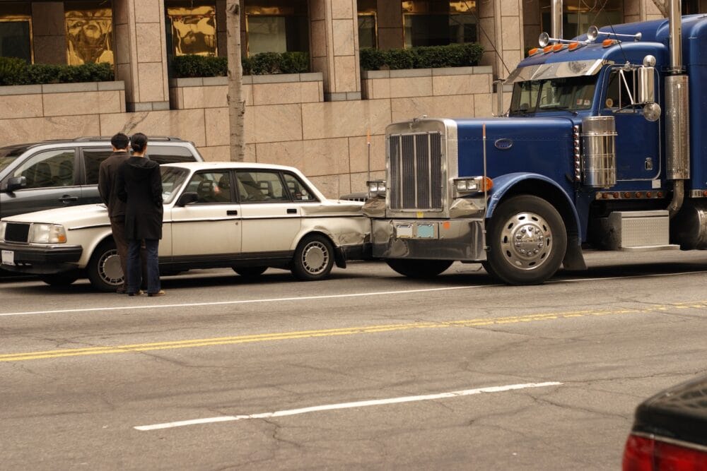 A blue semi truck rear-ended a smaller white car on the city streets.