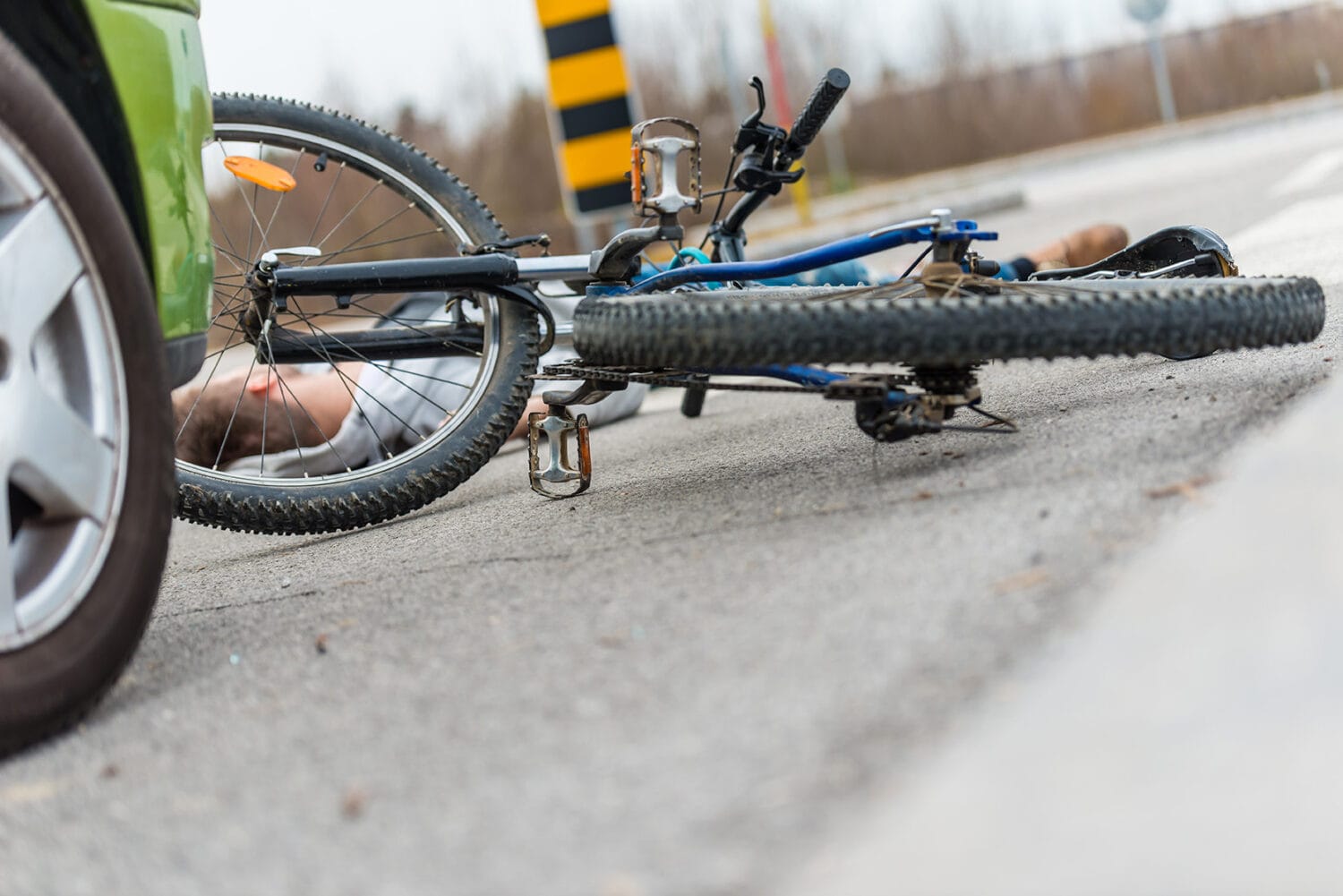 A crashed bicycle rider on the road in front of a green car.