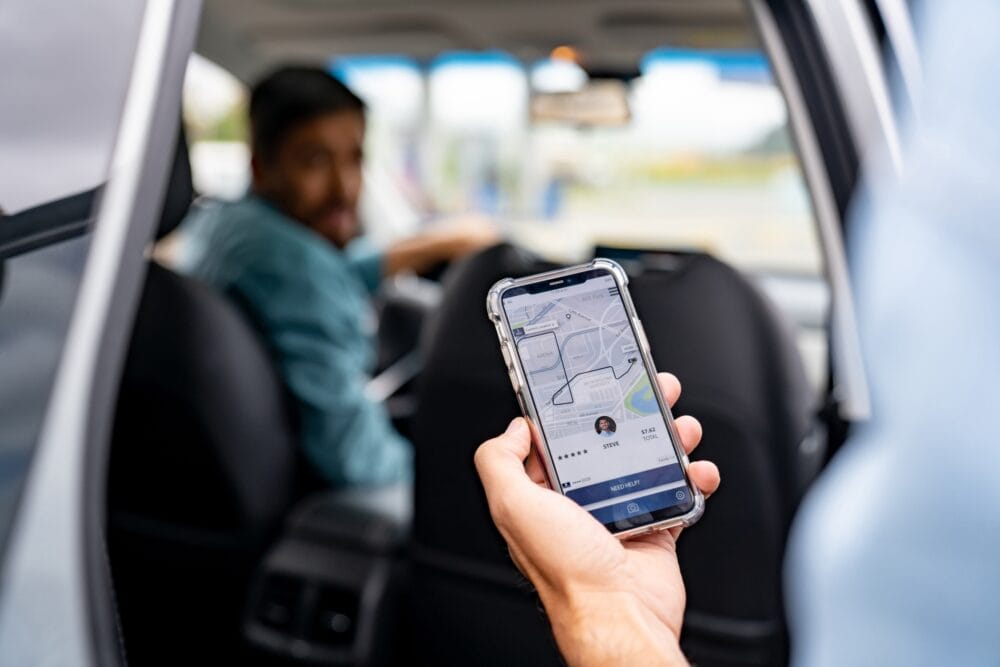 A rideshare passenger holding their phone as they open the door to their ride, talking to the driver.