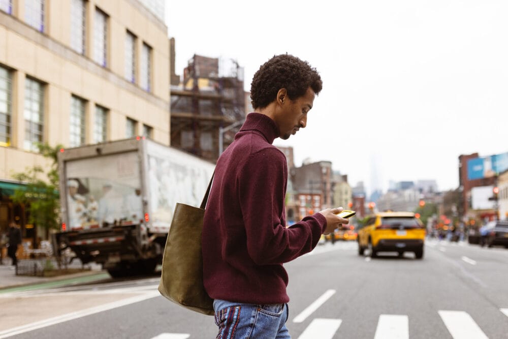 Young man crossing a city street while looking at his phone.