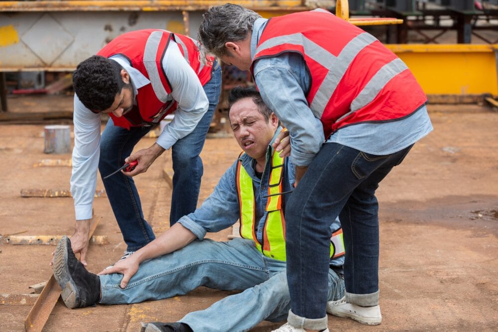 A hurt construction worker being helped by coworkers after a workplace accident.