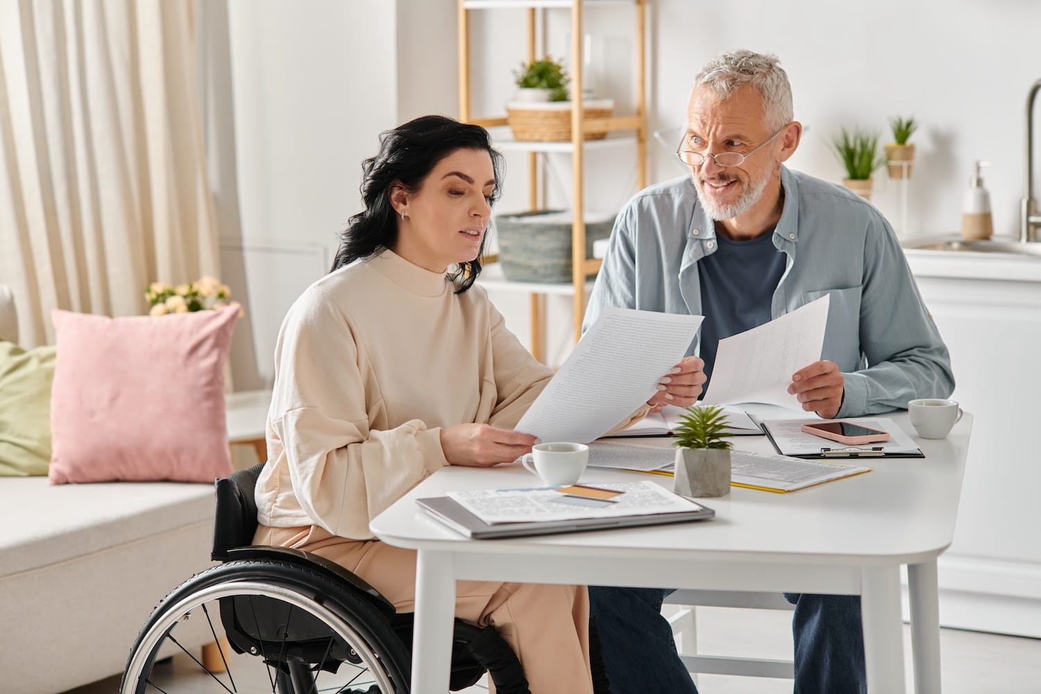 Disabled woman in wheelchair sits at table and reviews paperwork with husband.