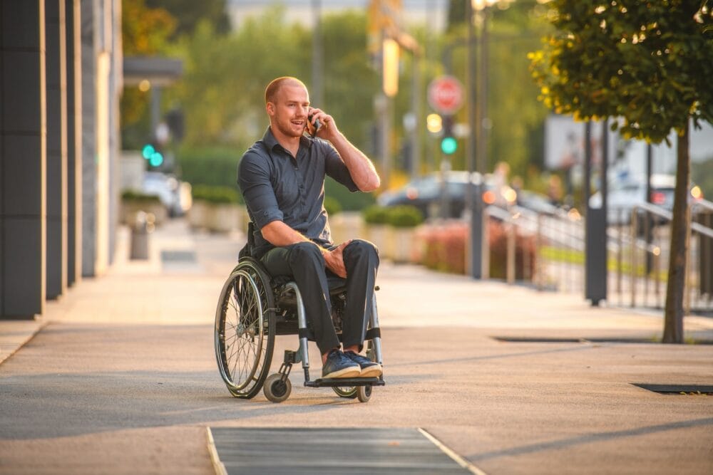 A man in a wheelchair is talking on the phone on a city sidewalk.