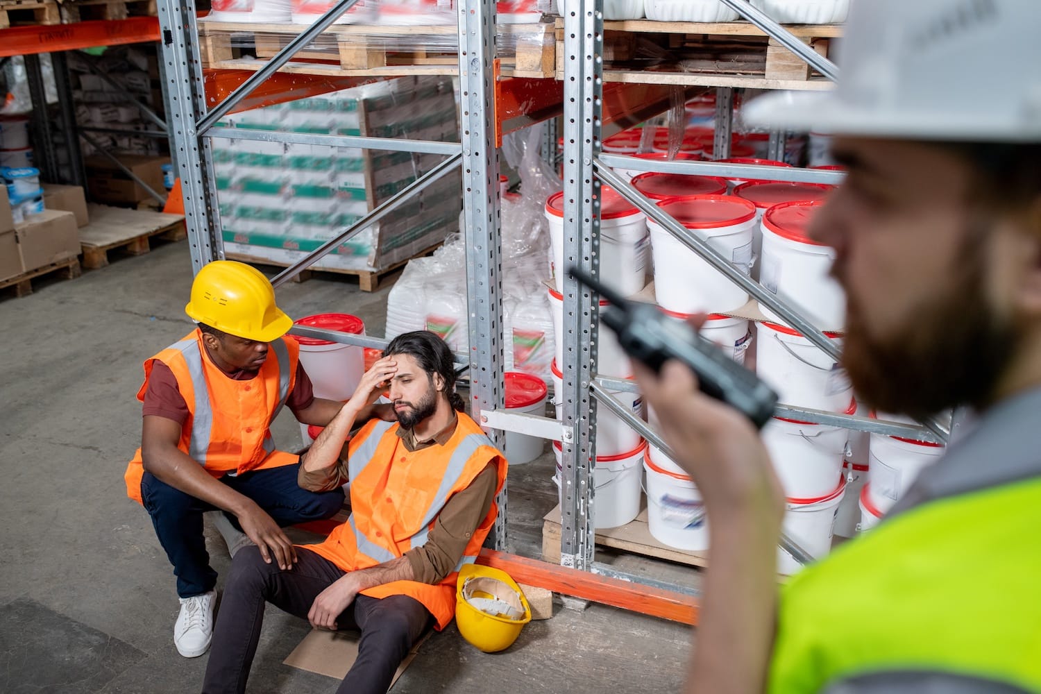 Warehouse worker assists an injured coworker while the supervisor calls for help.