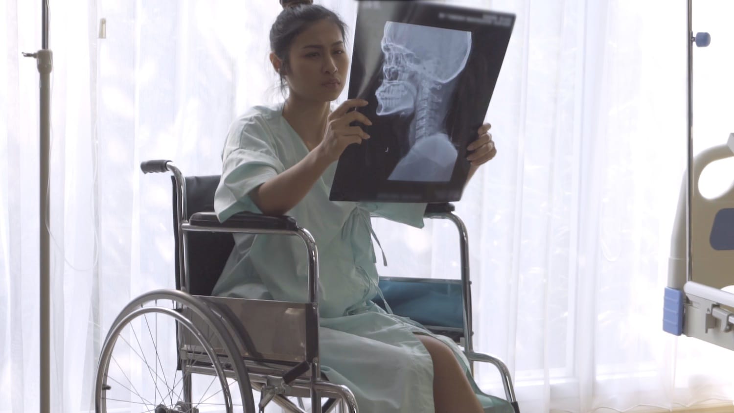 Woman in wheelchair examines head X-ray while sitting next to hospital bed.